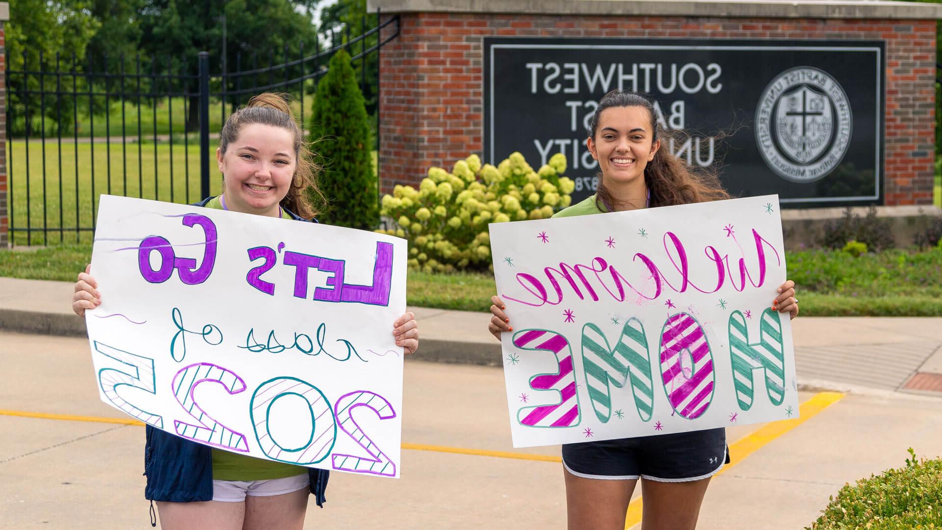学生们举着写着“欢迎回家”的牌子站在S-B-U正门前